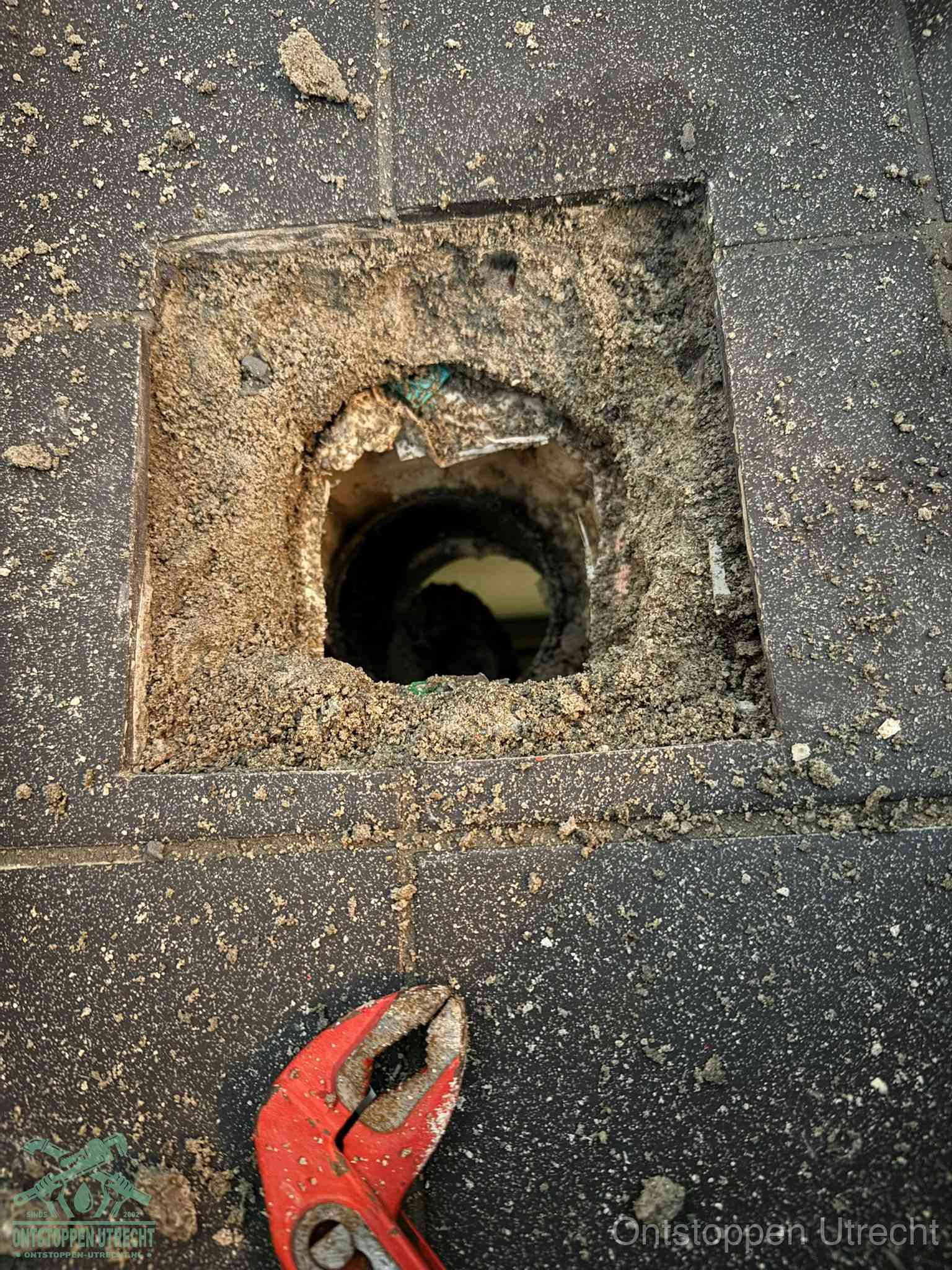 Een geopend rioolputje in een betontegelvloer met losgemaakt rooster en een zichtbare ronde afvoerbuis, het achterhalen waar de afvoerverstopping zit in Utrecht