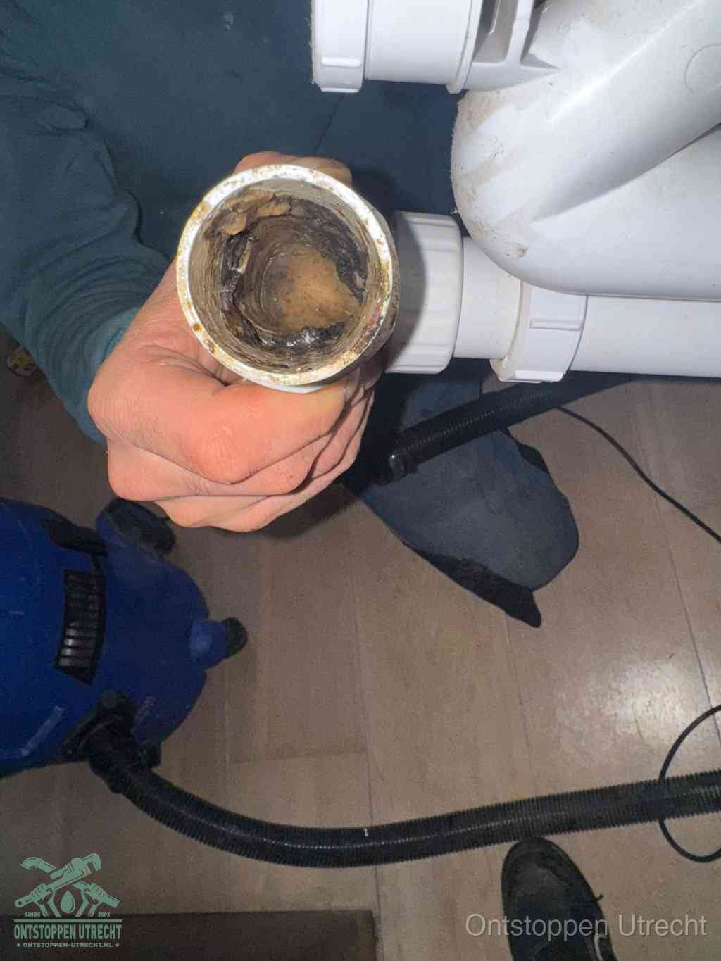 Een hand houdt een losgekoppeld PVC-afvoerbuisstuk vast dat van binnen volledig is dichtgeslibd met vet, vuil en aanslag, de meest voorkomende oorzaak van een verstopte afvoer in Utrecht