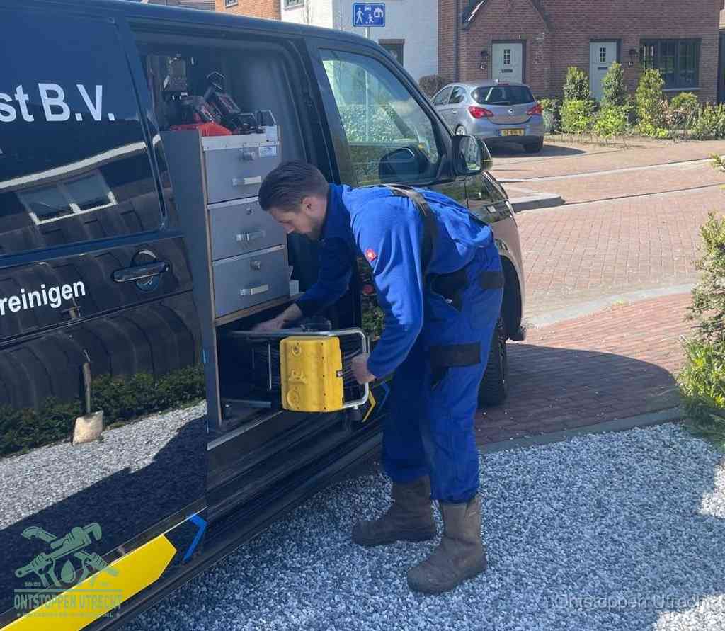 Een monteur pakt buiten op de oprit gereedschap uit de bedrijfsbus, het moment om een professional in te schakelen voor een verstopte afvoer in Utrecht