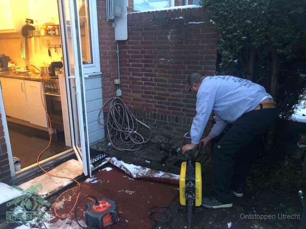 Een monteur werkt buiten bij een open riool-/grondput met een elektrische ontstoppingsmachine om een verborgen afvoerprobleem op te sporen in Utrecht