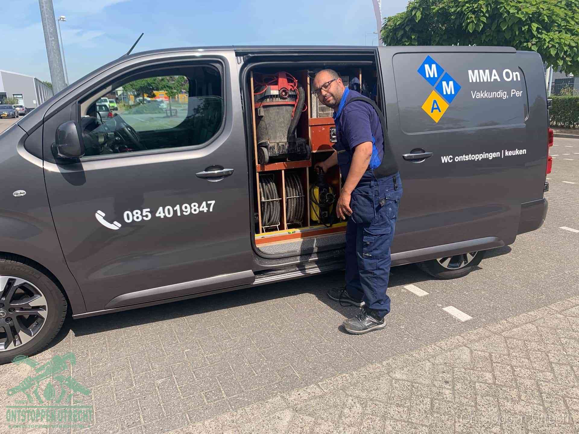 Een monteur bij de open schuifdeur van zijn bedrijfsbus op een parkeerplaats, klaar om de oorzaak van terugkerende afvoerverstoppingen aan te pakken in Utrecht