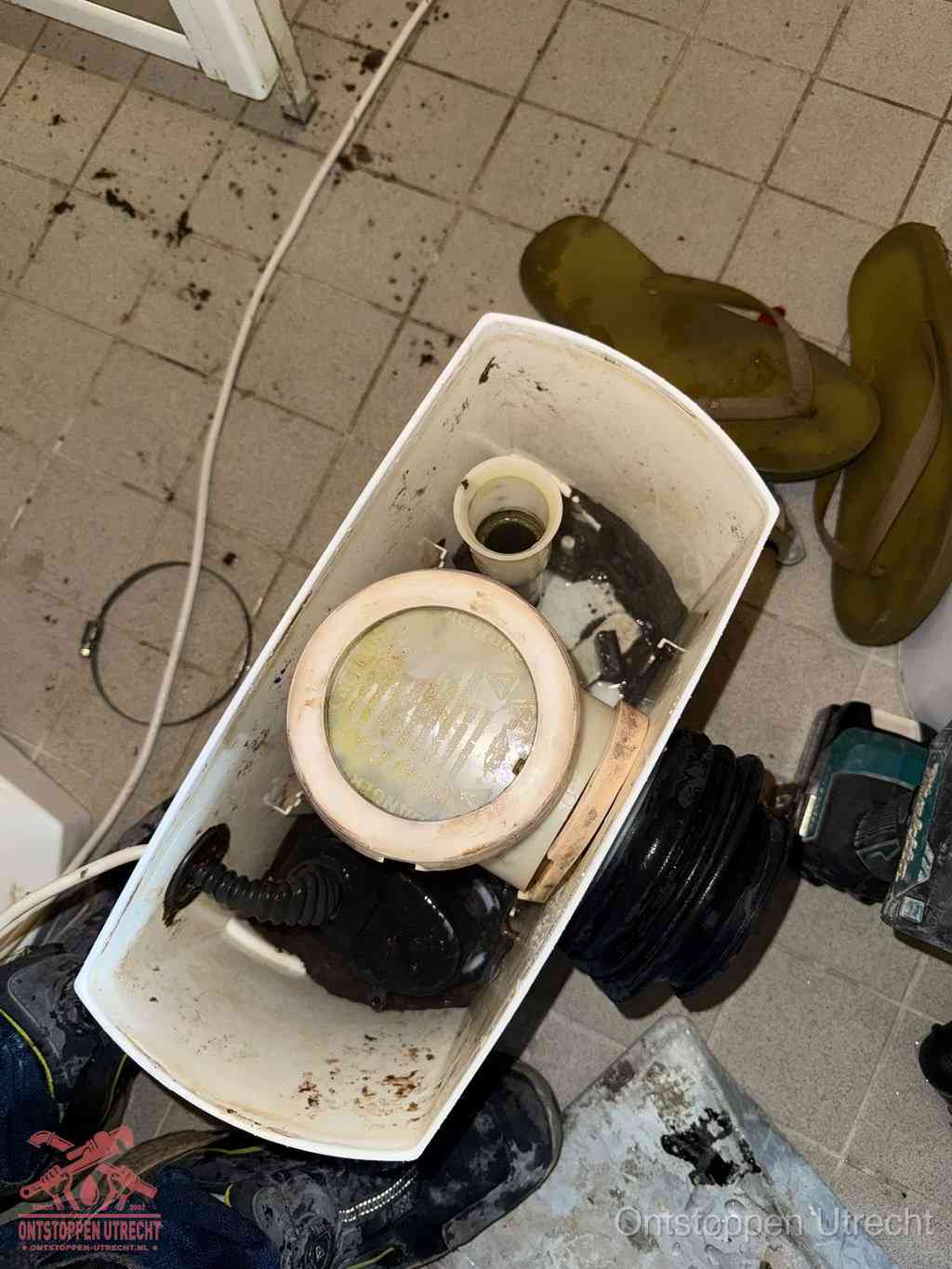 Een gedemonteerde toiletpot op de vloer met ontstoppingsveer en gereedschap ernaast, het verwijderen van een vastzittend voorwerp uit de wc in Utrecht