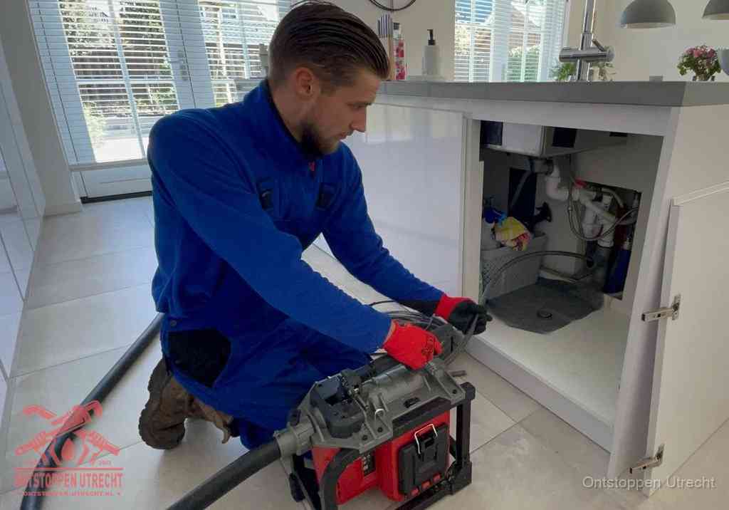 Een monteur voert een professionele elektrische ontstoppingsmachine in de afvoer onder de spoelbak tijdens het gootsteen ontstoppen in Utrecht